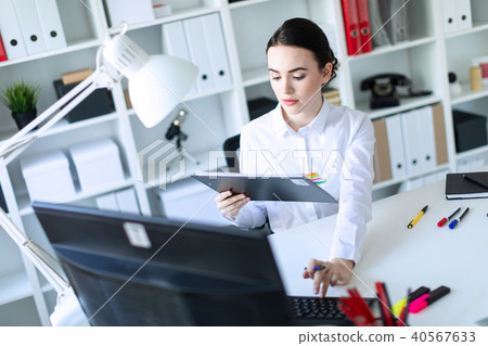 A young girl in the office holds a pen in her hand and works with documents and a computer. 40567633