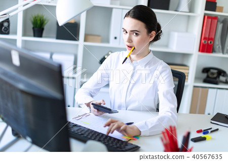 A young girl in the office holds a pen in her mouth and works with a calculator, documents and a 40567635