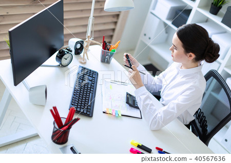 A young girl in the office sits at a table, holds a marker and a pencil in her hand and works with a 40567636