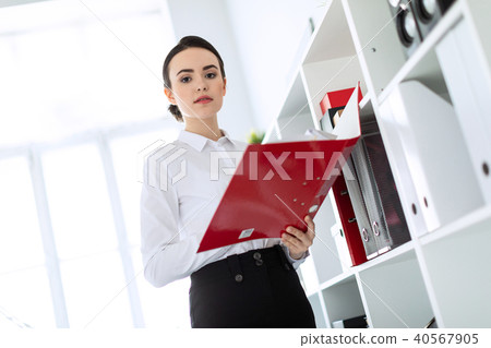 Young girl in the office near the rack and scrolls through the folder with the documents. 40567905