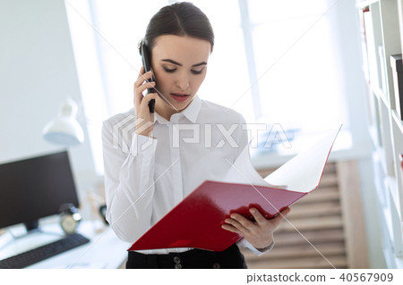 Young girl in the office near the rack and scrolls through the folder with the documents and speaks 40567909