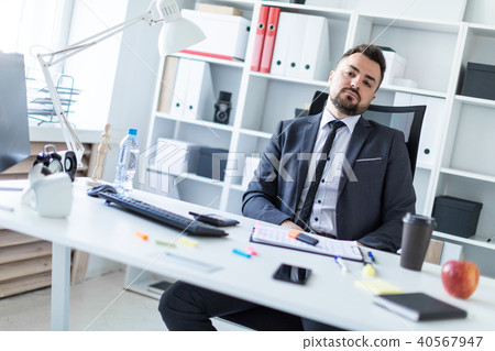 A man is sitting in a chair in the office at the table. 40567947