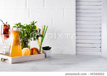 Orange lemonade in the decanter on a wooden tray with ftuits and mint 40568002