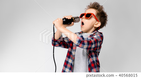 A handsome boy in a plaid shirt, gray shirt and jeans stands on a gray background. A boy wearing 40568015