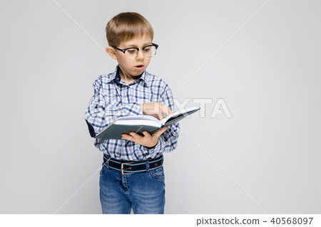 A charming boy with an inlaid shirt and light jeans stands on a gray background. The boy is holding 40568097