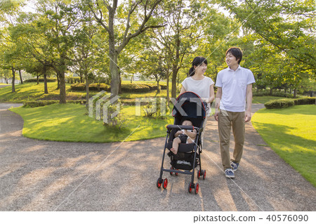 Young couple taking a walk while holding a stroller in fresh green park 40576090