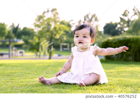 Baby girl sitting alone on the park lawn and playing Baby girl sitting alone on the park lawn and playing 40576252
