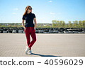 Stylishly dressed young woman in glasses stands in the middle of a stone square against the 40596029