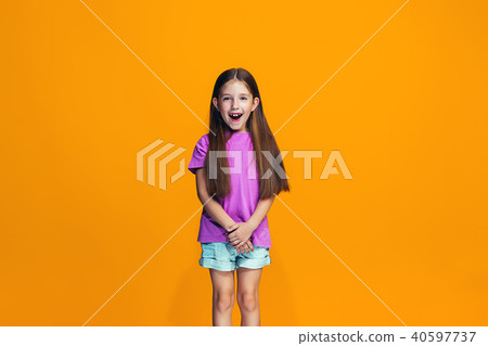 The happy teen girl standing and smiling against orange background. 40597737