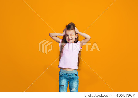 The happy teen girl standing and smiling against orange background. 40597967