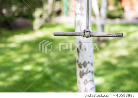 Wooden single rope swing in garden on bright sunny day. Green grass lawn on background. Children 40598985