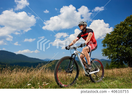 Professional sportsman rider in sportswear and helmet cycling bicycle in high grass 40610755