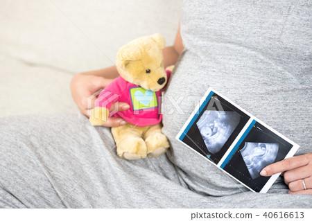 Pregnant woman sitting on sofa holding ultrasound. 40616613
