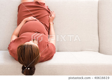 Young pregnant woman sitting on gray sofa top view Young pregnant woman sitting on gray sofa top view 40616619