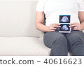 Pregnant woman sitting on sofa holding ultrasound. 40616623