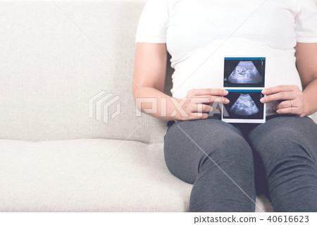 Pregnant woman sitting on sofa holding ultrasound. Pregnant woman sitting on sofa holding ultrasound. 40616623