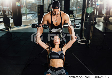 Sporty girl doing weight dumbbells exercises with assistance of her personal trainer at public gym. Sporty girl doing weight dumbbells exercises with assistance of her personal trainer at public gym. 40624937