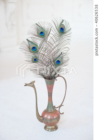 Vintage ancient copper jug on white table decorated with big peacock feather Vintage ancient copper jug on white table decorated with big peacock feather 40626538