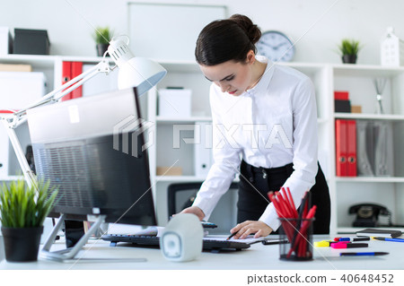 A young girl in the office is standing near the table, holding a pencil and a calculator in her hand 40648452