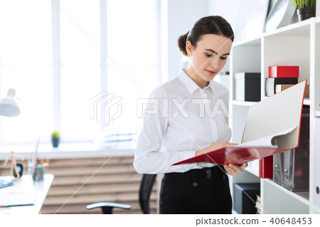 Young girl in the office near the rack and scrolls through the folder with the documents. 40648453