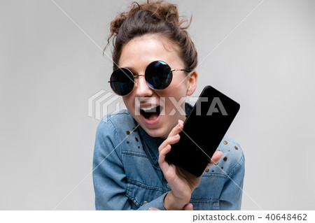 Young brunette girl in round glasses. Hairs are gathered in a bun. Girl with a black phone. 40648462
