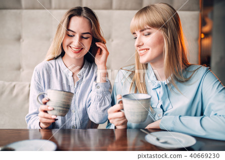 Two smiling girlfriends drinks coffee in cafe 40669230