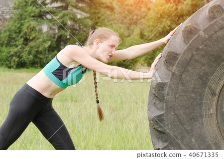 Girl in sportswear pussh a tire. Street workout. 40671335