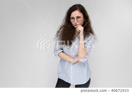 Young brunette girl with glasses. The girl put a finger to her cheek. 40672933