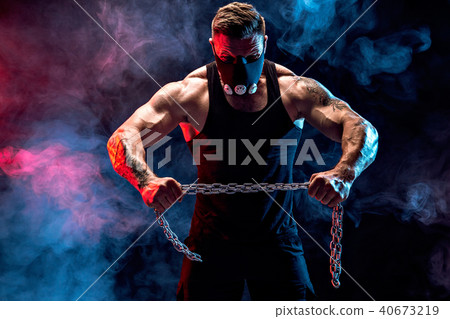 Portrait of muscular sportsman tearing metal chain. Black background with smoke 40673219