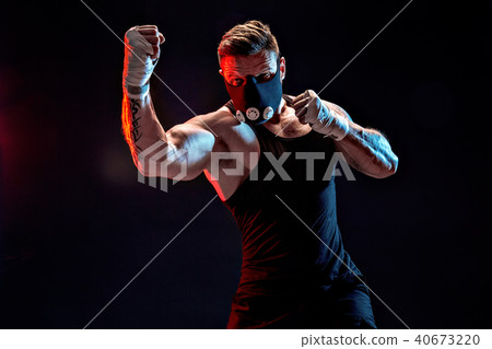 Strong male athlete in a black training mask on a black background 40673220