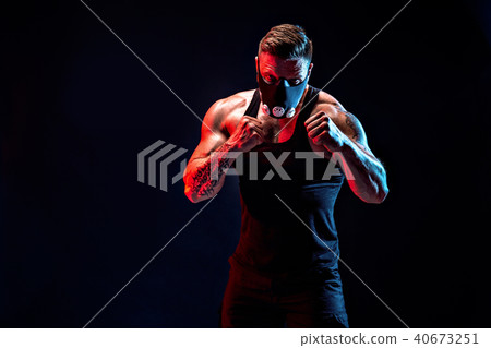 Strong male athlete in a black training mask on a black background Strong male athlete in a black training mask on a black background 40673251