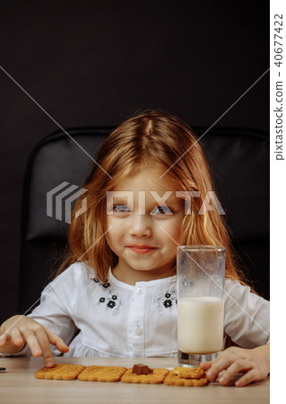 Happy beautiful little girl having a snack with milk and cookies 40677422