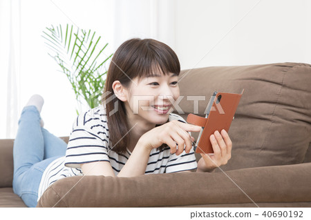A young lady who operates a smartphone lying on the sofa 40690192