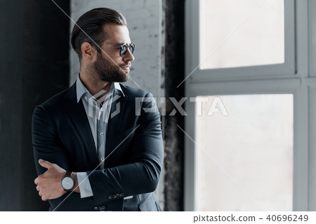 Young stylish businessman leader indoors at office in sunglasses walking looking aside 40696249