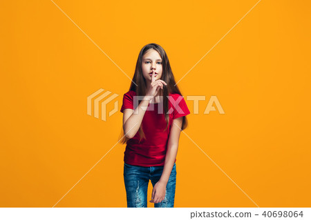 The young teen girl whispering a secret behind her hand over orange background The young teen girl whispering a secret behind her hand over orange background 40698064