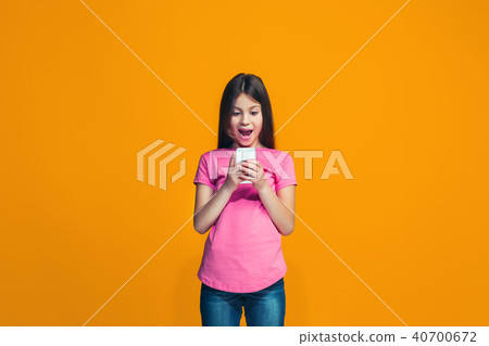The happy teen girl standing and smiling against orange background. 40700672