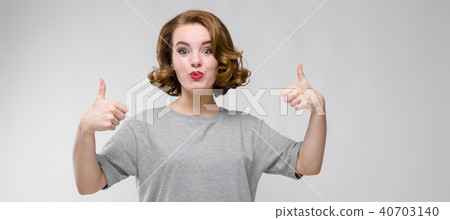 Charming young girl in a gray T-shirt on a gray background. The girl shows class Charming young girl in a gray T-shirt on a gray background. The girl shows class 40703140