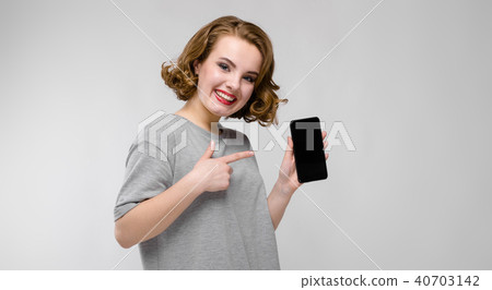 Charming young girl in a gray T-shirt on a gray background. A girl is holding a phone in her hand Charming young girl in a gray T-shirt on a gray background. A girl is holding a phone in her hand 40703142