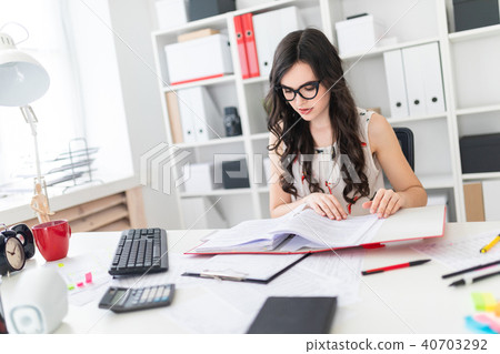 Beautiful young girl sits at office desk and scrolls through a folder with documents. Beautiful young girl sits at office desk and scrolls through a folder with documents. 40703292