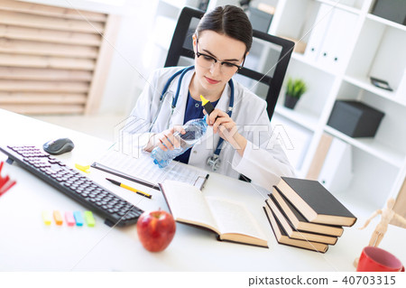 A beautiful young girl in a white robe sits at a computer desk, holds a marker in her hand and opens 40703315