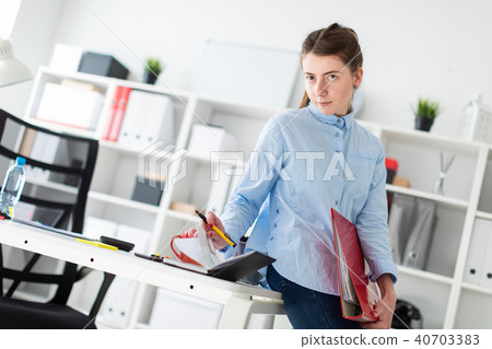 A young girl in the office is standing, leaning on a table, and writing in a diary. 40703383