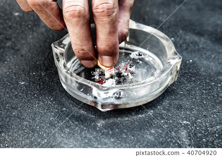 hand with a cigarette butt stubbed out amidst ash 40704920