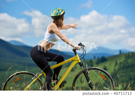 Young happy woman riding bicycle in the mountains at summer day Young happy woman riding bicycle in the mountains at summer day 40711713