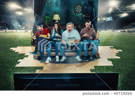 Soccer football fans sitting on the sofa and watching TV in the middle of a football field. Soccer football fans sitting on the sofa and watching TV in the middle of a football field. 40719269