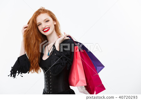 Halloween witch concept - Happy Halloween Witch smiling and holding colorful shopping bags on white Halloween witch concept - Happy Halloween Witch smiling and holding colorful shopping bags on white 40720293