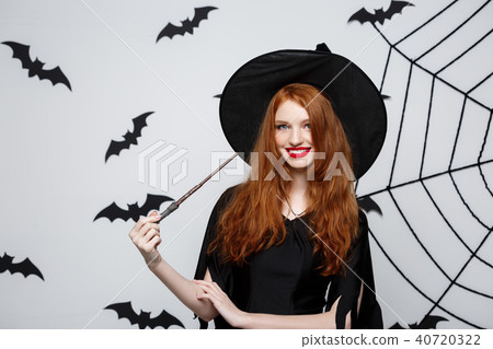 Halloween Concept - Beautiful Witch playing with magic stick on grey background. Halloween Concept - Beautiful Witch playing with magic stick on grey background. 40720322