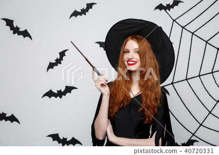 Halloween Concept - Beautiful Witch playing with magic stick on grey background. Halloween Concept - Beautiful Witch playing with magic stick on grey background. 40720331