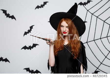 Halloween Concept - Beautiful Witch playing with magic stick on grey background. Halloween Concept - Beautiful Witch playing with magic stick on grey background. 40720345