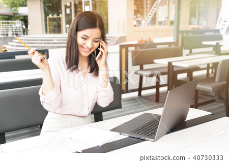 Young pretty woman speaking on mobile phone and sitting in cafe with notebook. 40730333