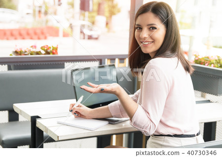 Young female student in cafe working on laptop turned back and asking. Young female student in cafe working on laptop turned back and asking. 40730346